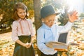 Little boy 6, 7 years old with hat, glasses, reading a book and girl 7, 8 years old, together in the autumn sunny park, golden hou Royalty Free Stock Photo