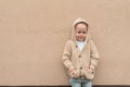 Little boy 3-5 years old, stands in autumn beige wall, in warm casual clothes, sweater with hood, happy smiling, free Royalty Free Stock Photo