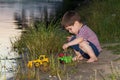 A little boy of 3 years plays on the river bank with bright toys, digs sand. Children`s games near the pond in the fresh air in Royalty Free Stock Photo