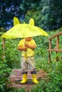 A little boy in yellow boots hides under a yellow umbrella. rain