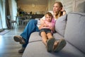 Little braided girl leaning on mother& x27;s laps sitting on sofa