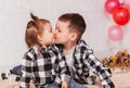 Little brother and sister kiss in a room with multicolored inflatable balloons