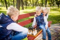 Little brothers playing chess with sister on bench in park. Children intelligence development. Family leisure time. Kids playing Royalty Free Stock Photo