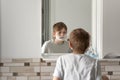 Little brunette boy applies shaving foam to face. Reflection in the mirror. Child is fun in bathroom Royalty Free Stock Photo