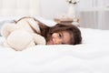 Little brunette girl lying with teddy bear on bed at home