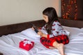 Little brunette girl in pajamas lies on the bed at home, looks into the digital tablet Royalty Free Stock Photo