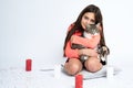 Little brunette girl sitting on the pillow, hugging a cat and looking at the camera, red and white candles are placed Royalty Free Stock Photo