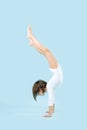 Fit little girl in a white leotard doing handstand over blue background Royalty Free Stock Photo