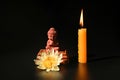 A little Buddha statue, water lily, and burning candles on black background Royalty Free Stock Photo