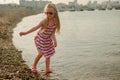 little calm girl in a dress and sunglasses walks into the sea water on the pebble coast