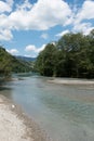 Little calm turquoise river with trees on shore and mountains in the background