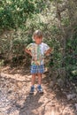 Little candid tired kid boy traveler and hiker of five years old in shorts and a t-shirt travels and hiking a mountain path among Royalty Free Stock Photo