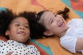 Little Caucasian and African kids girls smiling laughing and lying together on colorful mat on green grass. Royalty Free Stock Photo