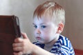 Little caucasian baby boy uses a tablet, seeing to the screen. Children time spending, computerization of youngsters. Royalty Free Stock Photo