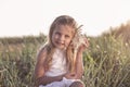 Little caucasian blond girl holding seashell and listening to the sea sitiing on grass field