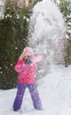 Little Caucasian blond girls in red jacket is playing with snow on fir-tree blur background