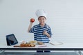 A little Caucasian boy chef with tablet to prepare food for cooking in studio kitchen Royalty Free Stock Photo