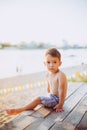 Little Caucasian boy child sitting on wooden pier sandy beach, summer time, sea vacation near water. The theme is the flow of time Royalty Free Stock Photo