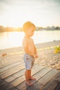 Little Caucasian boy child sitting on wooden pier sandy beach, summer time, sea vacation near water. The theme is the flow of time Royalty Free Stock Photo