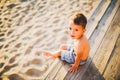 Little Caucasian boy child sitting on wooden pier sandy beach, summer time, sea vacation near water. The theme is the flow of time Royalty Free Stock Photo