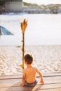 Little Caucasian boy child sitting on wooden pier sandy beach, summer time, sea vacation near water. The theme is the flow of time