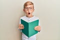 Little caucasian boy kid reading a book wearing glasses afraid and shocked with surprise and amazed expression, fear and excited Royalty Free Stock Photo