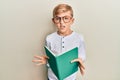 Little caucasian boy kid reading a book wearing glasses clueless and confused expression Royalty Free Stock Photo