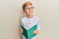 Little caucasian boy kid reading a book wearing glasses smiling looking to the side and staring away thinking Royalty Free Stock Photo