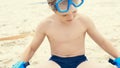 Little Caucasian boy with snorkeling equipment sitting on sand on tropical beach and playing with flippers on hands. Royalty Free Stock Photo
