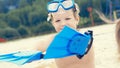 Little Caucasian boy with snorkeling equipment sitting on sand on tropical beach and playing with flippers on hands. Royalty Free Stock Photo