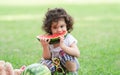 Little Caucasian cute girl holding sliced watermelon and enjoy eating or biting while picnic at park. Happy healthy child sitting Royalty Free Stock Photo