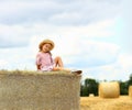 Little caucasian cute girl smiles in a wicker hat and a pink blue dress on a huge haystack on a mown wheat field. Agriculture. Royalty Free Stock Photo