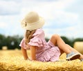 Little caucasian cute girl smiles in a wicker hat and a pink blue dress on a huge haystack on a mown wheat field. Agriculture. Royalty Free Stock Photo