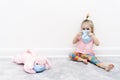 Little Caucasian Girl Baby In Facial Protective Mask Sits At Home At Quarantine With Pink Dog Toy