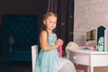 caucasian girl in a blue dress sits on a chair at the dressing table and holds pink beads in her hands Royalty Free Stock Photo