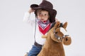 Little Caucasian Girl in Cowgirl Clothing Posing On Symbolic Horse Against White. Holding Her Stetson