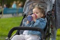 Little Caucasian girl dressed in a denim jacket drinks juice from her bottle while sitting in a baby carriage Royalty Free Stock Photo