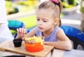 Little caucasian girl eating rench fries with sauce at street cafe outside. Royalty Free Stock Photo