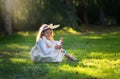 Little Caucasian girl in festive dress and bunny ears headband sitting on green grass and playing with Easter eggs Royalty Free Stock Photo