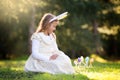 Little Caucasian girl in festive dress and bunny ears headband sitting on green grass and playing with Easter eggs Royalty Free Stock Photo