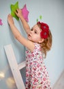 Little Caucasian girl in a floral print dress climbs a wooden ladder behind the stars