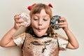 Little caucasian girl kid holding tasty colorful doughnuts making fish face with mouth and squinting eyes, crazy and comical