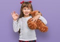 Little caucasian girl kid hugging teddy bear stuffed animal doing ok sign with fingers, smiling friendly gesturing excellent Royalty Free Stock Photo