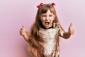 Little caucasian girl kid wearing festive sequins dress success sign doing positive gesture with hand, thumbs up smiling and happy