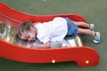 Little Caucasian girl lies on a slide at the playground tired of a sad summer day Royalty Free Stock Photo