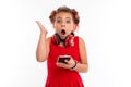 Little caucasian girl listens to music with big red earphones isolated on white background