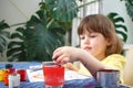 Little caucasian girl paints small toy figures in home interior. A cute three year old child is engaged in creativity Royalty Free Stock Photo