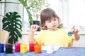 Little caucasian girl paints small toy figures in home interior. A cute three year old child is engaged in creativity Royalty Free Stock Photo