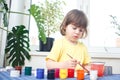 Little caucasian girl paints small toy figures in home interior. A cute three year old child is engaged in creativity Royalty Free Stock Photo