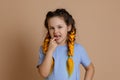 Little Caucasian girl putting fingers in mouth showing missing tooth looking at camera having kanekalon braids on head